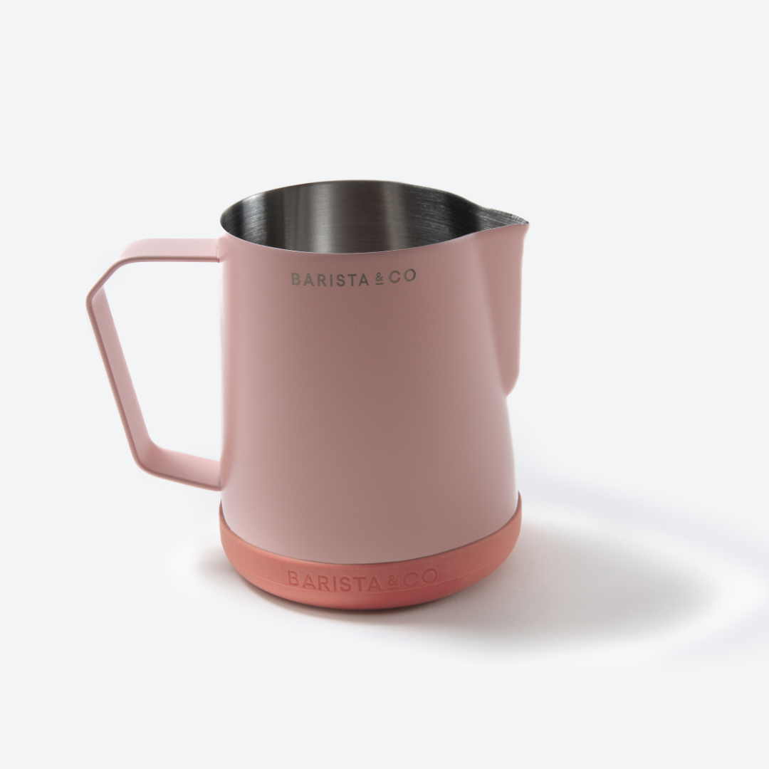 A Barista & Co stainless steel milk pitcher with a matte dusty pink body, a matching pink handle, and a darker pink silicone base, shown on a clean white background.