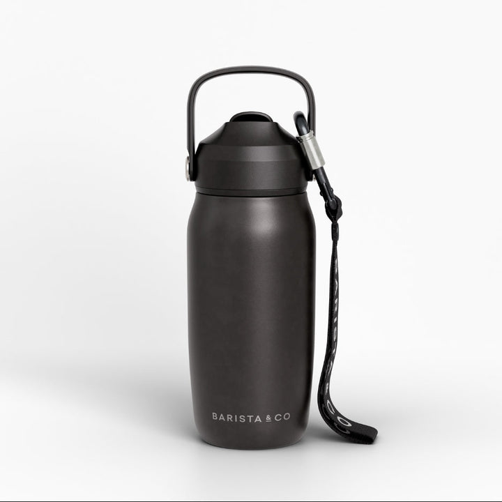 A matte black insulated water bottle with a carrying loop and wrist strap, featuring the BARISTA & CO logo near the base, set against a clean white background.