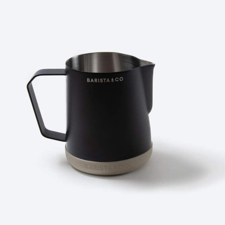 A matte black stainless steel latte pitcher with a handle and spout, featuring the BARISTA & CO logo printed in white on the side, set against a clean white background.