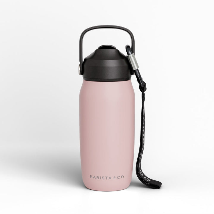 A light pink insulated water bottle with a black lid, carrying loop, and black wrist strap, shown on a clean white background. The brand name 'BARISTA CO' is printed near the bottom.
