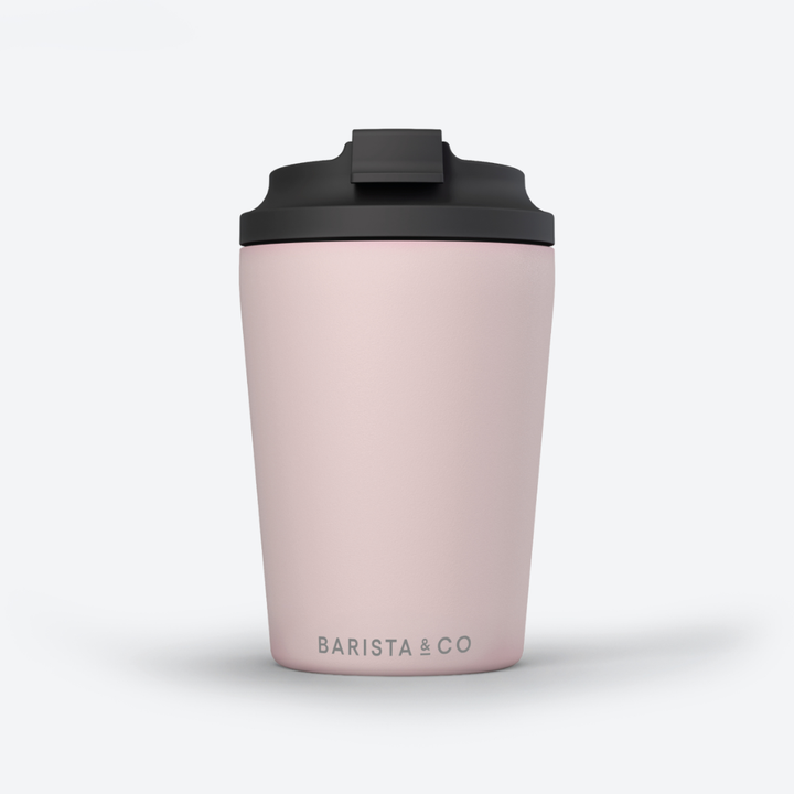 A light pink travel tumbler with a black lid, featuring the 'BARISTA & CO' logo printed in gray near the bottom, set against a clean white background.