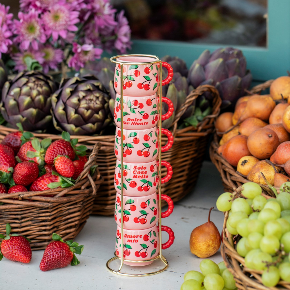 Stack of pink mugs with cherry design on a table with fruits and flowers