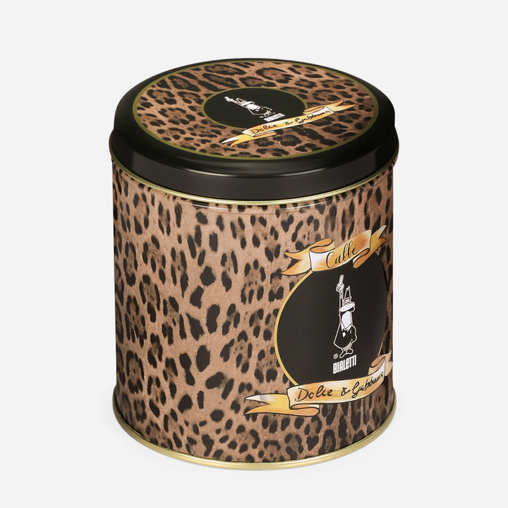 A cylindrical metal tin with a leopard print pattern, black lid, and gold accents. The front features a black oval label with a white illustration of a coffee cup and the text 'Caffè Dolce & Gabbana'.